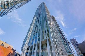 Toronto (Annex) condo for rent - A tall glass building stands under a blue sky.
