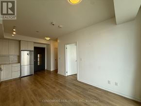 Toronto (Henry Farm) condo for rent - A spacious room with wood flooring and white walls, featuring a kitchen area with a refrigerator and cabinets.