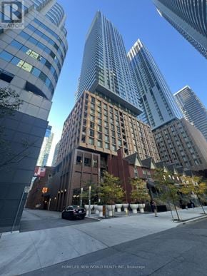 Toronto (Waterfront Communities) condo for rent - A tall building with a glass facade stands in front of a smaller building with a brick facade.