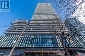 Toronto (Waterfront Communities) condo for rent - A tall building with a glass facade and a tree in front of it.