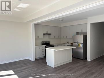 Kawartha Lakes (Lindsay) townhouse for rent - A kitchen with white cabinets and a white island with a stainless steel refrigerator.