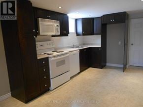Toronto (Wexford-Maryvale) apartment for rent - A kitchen with a white stove top oven and microwave, and black cabinets.