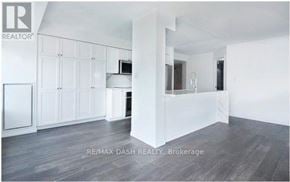 Toronto (Niagara) condo for rent - A spacious room with white walls and wooden flooring, featuring a kitchen area with white cabinets and a countertop.