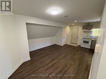 Guelph (Exhibition Park) apartment for rent - A room with wooden flooring and white walls, with a kitchen area visible in the background.