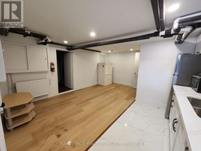 Toronto (Annex) multi-family for rent - A room with wooden flooring and white walls, with a kitchen area to the right.