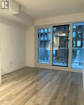 Toronto (Kensington-Chinatown) condo for rent - A room with wooden flooring and a large window with a view of a building outside.