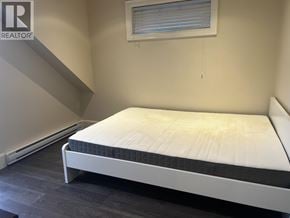 Vancouver apartment for rent - A bed with a white mattress and a grey headboard is in a room with a window.