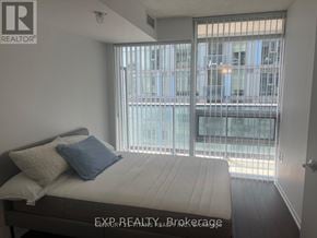 Toronto (Little Portugal) condo for rent - A bedroom with a bed, pillows, and a window with a view of a cityscape.