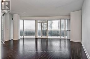 Toronto (Mimico) condo for rent - A spacious room with wooden floors and large windows overlooking a cityscape.