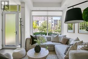 Toronto (Kensington-Chinatown) townhouse for rent - A living room with a grey couch, a white coffee table, and a large window with a view of the city.