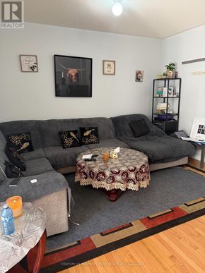 Brampton (Credit Valley) apartment for rent - A living room with a grey couch, a round table with a floral tablecloth, and a rug on the floor.