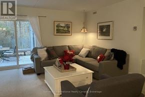 Collingwood townhouse for rent - A living room with a grey couch, a white coffee table, and a large window with a view of trees outside.