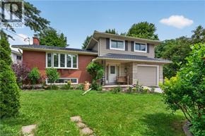 Kitchener apartment for rent - A house with a red brick exterior and a grey roof is surrounded by a green lawn and trees.