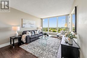 Brampton (Queen Street Corridor) condo for rent - A living room with a black couch, a glass coffee table, and a large window with a view of the outdoors.