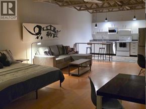 Vancouver apartment for rent - A bedroom with a bed, couch, and a kitchen area in the background.