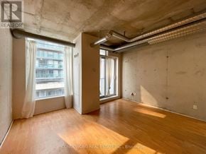 Toronto (Little Portugal) condo for rent - A large empty room with wooden floors and a window with white curtains.