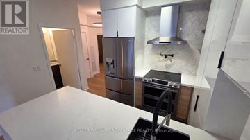 Toronto (Regent Park) condo for rent - A modern kitchen with a stainless steel refrigerator and a black stove top.