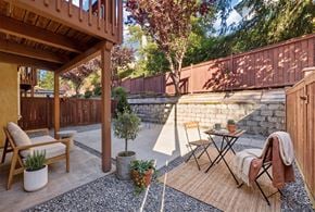 Bellevue apartment for rent - Private ground-level patio with a cedar fence, stone retaining wall, lounge chair, and bistro table under a wood deck.