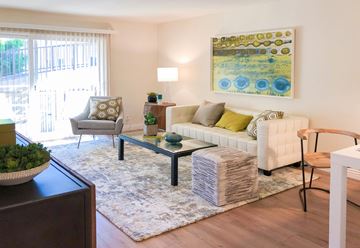 Mountain View apartment for rent - A living room with a white couch, a grey chair, a glass coffee table, and a painting on the wall.