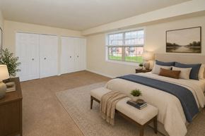 Reisterstown apartment for rent - A bedroom with a large bed and a window overlooking a green area.