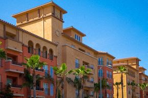 Los Angeles apartment for rent - A building with a red and beige facade with balconies and palm trees in front.