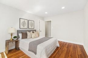 Orange apartment for rent - A bedroom with a bed, a lamp, and two framed leaves on the wall.