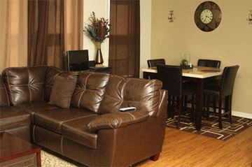 Chicago apartment for rent - A brown leather couch in a living room with a dining table and chairs in the background.