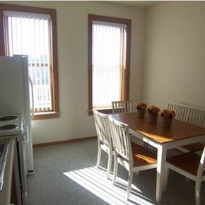 Spirit Lake apartment for rent - A white dining table with four chairs and a refrigerator in a room.