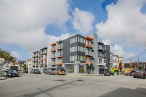 San Francisco apartment for rent - A modern multi-story building with orange accents is situated on a street corner with cars parked in front.