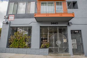 San Francisco apartment for rent - A grey building with a red sign on the left and a balcony on the right.