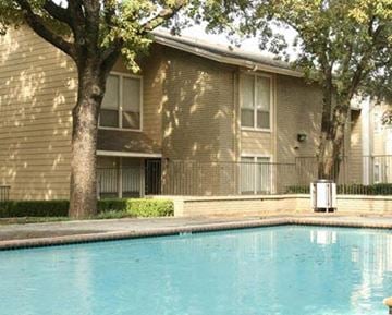 Hurst apartment for rent - A pool in front of a tan building with a tree in front of it.