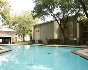 Hurst apartment for rent - A swimming pool in front of a building surrounded by trees.
