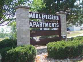 Mora apartment for rent - a sign evergreen apartments in front of trees and bushes