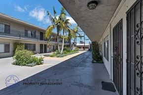 Anaheim apartment for rent - A long, narrow walkway between two buildings with a logo for Beachfront Property Management in the bottom left corner.