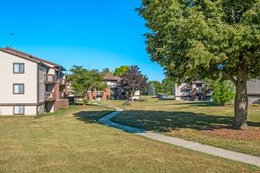 Grand Rapids apartment for rent - A grassy area with a tree and a pathway leading to apartment buildings.
