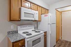 Wyoming apartment for rent - A kitchen with a white stove top oven, a white microwave, and a white refrigerator.
