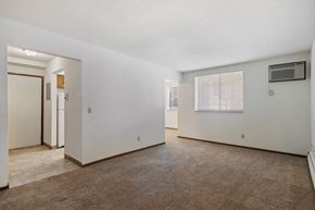 Grandville apartment for rent - A spacious, empty room with a carpeted floor and a window with blinds.