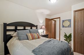 Comstock Park apartment for rent - A bedroom with a bed, pillows, a nightstand with a lamp, and a door.