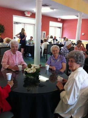 Pineville apartment for rent - A group of elderly people are sitting around a table in a room with red walls and white columns.