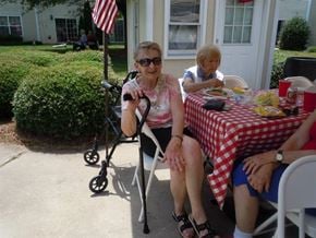 Pineville apartment for rent - An elderly woman in a pink floral dress sits at a table with a red and white checkered tablecloth.
