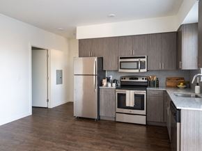 Seattle apartment for rent - Kitchen featuring wood-grain cabinets, stainless steel appliances, speckled countertops, and dark wood-style floors.