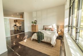 Seattle apartment for rent - Staged studio bedroom with bed, dresser, concrete floors, large windows, and open view into the kitchen.