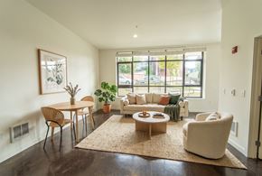Seattle apartment for rent - Living room with polished concrete floors, large multi-pane window, sofa, accent chair, and small dining table.