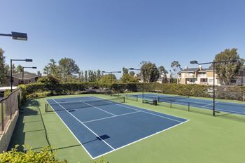 Two tennis courts with houses in the background on a sunny day