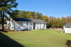 Tuscaloosa apartment for rent - A white building with a black roof is surrounded by a grassy field.