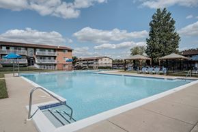 Laurel apartment for rent - A large swimming pool in front of a building with a blue sky and clouds in the background.