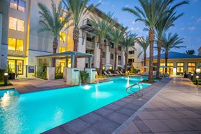 Scottsdale apartment for rent - A swimming pool surrounded by palm trees and a building in the background.