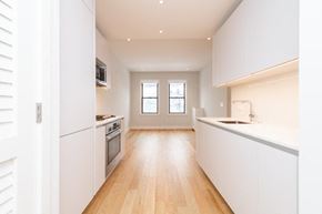 Brighton apartment for rent - an empty kitchen with white cabinets and a wood floor