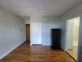 Chicago apartment for rent - a room with white walls and wood floors and a black refrigerator