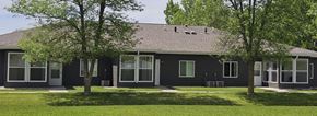 Fosston apartment for rent - A house with a grey roof and green trees in front.